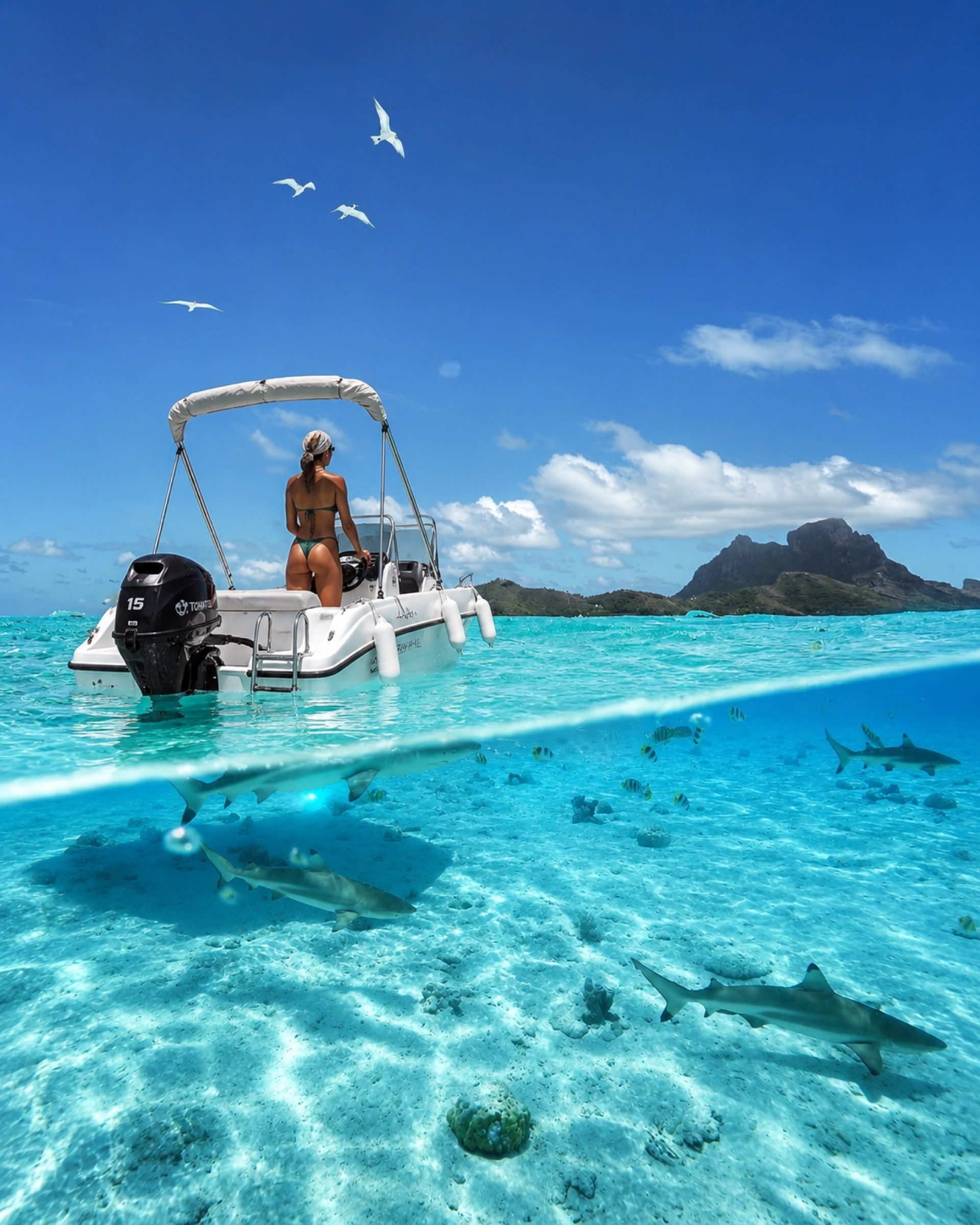A woman at the helm of the boat in a bright lagoon with an island peak behind
